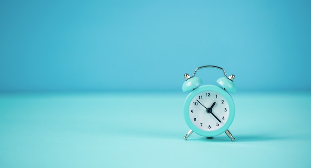 Blue small alarm clock on a blue background.