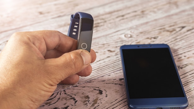 Blue smart bracelet in hand and blue smartphone on wooden table.