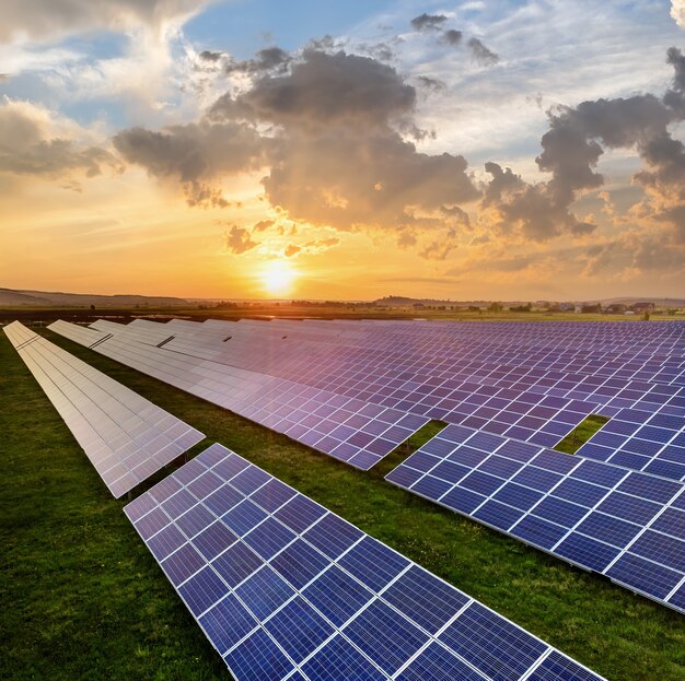 Pannelli fotovoltaici solari blu che producono energia pulita rinnovabile sul paesaggio rurale e sullo sfondo del sole al tramonto.