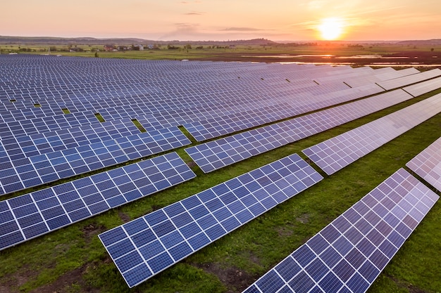 Голубая солнечная система фотоэлектрических панелей производит возобновляемую чистую энергию на фоне сельского пейзажа и заходящего солнца.