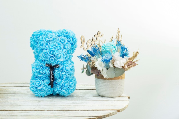 Blue souvenir gift bear made of plastic rose flowers and a flower arrangement of dried and preserved flowers on the table with the