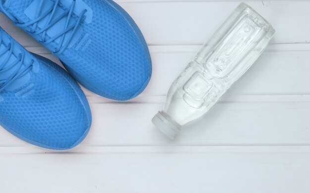 Blue sports shoes for running, bottle water on white wooden\
floor. top view.