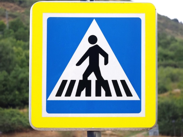 A blue square in a yellow frame featuring a pedestrian crossing a zebra striped crosswalk
