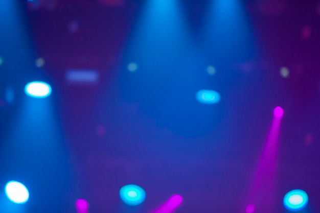 Blue stage background with white and pink projector beams.