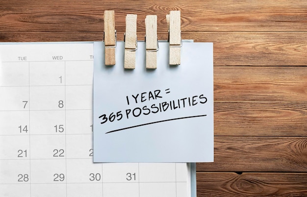 Фото Синяя наклейка прикреплена к календарю на деревянном фоне с текстом 1 год 365 возможностей