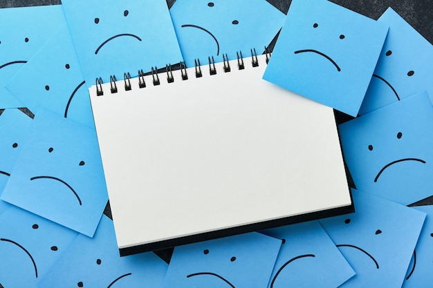 Blue sticky notes blank with drawing sad face on black background with copy space ready for your message Blue Monday and mental health concept idea Flat lay copy space on black background