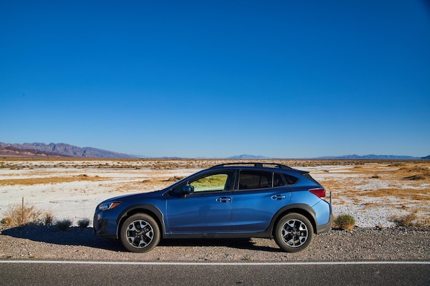 Blue Subaru Crosstrek은 데스 밸리 외부의 배경에 하얀 모래 사막이 있는 도로에 주차되어 있습니다.