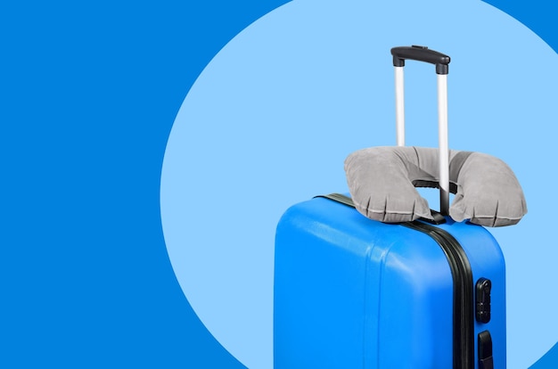 Blue suitcase and travel pillow on a blue background