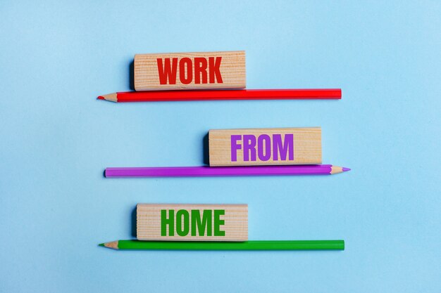 On a blue surface, three colored pencils, three wooden blocks with text WORK FROM HOME