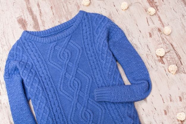 Photo blue sweater and garland on a wooden surface