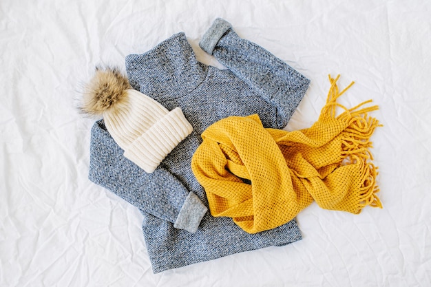 黄色のニットスカーフと帽子が付いた青いセーター。白い背景の上の秋/冬のファッションの服のコラージュ。上面図フラットレイ。