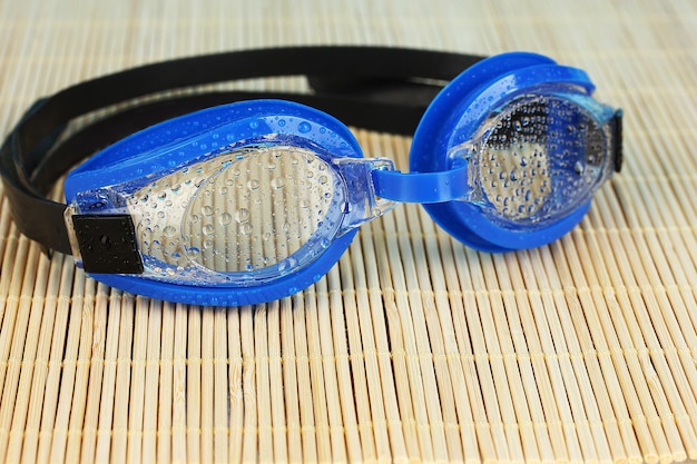 Blue swim goggles with drops on a bamboo pad