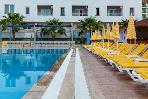 Blue swimming pool with yellow sun loungers and parasols for relaxing