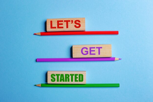 On a blue table, three colored pencils, three wooden blocks with text LETS GET STARTED