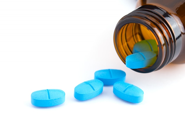 blue tablet of medicine spilling out of glass bottle on white 