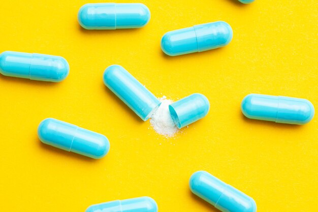 Blue tablets in capsules One capsule is open Yellow background