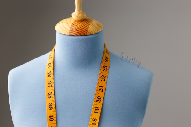 Blue tailor dummy with measuring tape alongside the wall.