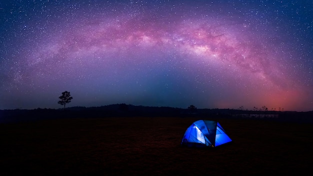 Blue tent glows under a night sky with milky way.