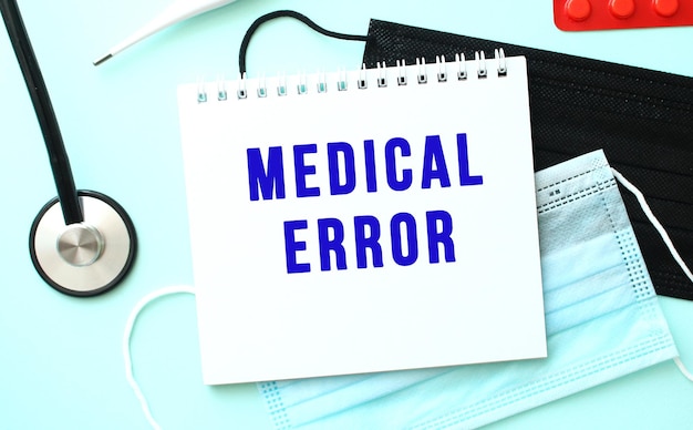 The blue text MEDICAL ERROR is written in a notebook that lies on a blue background next to a medical masks