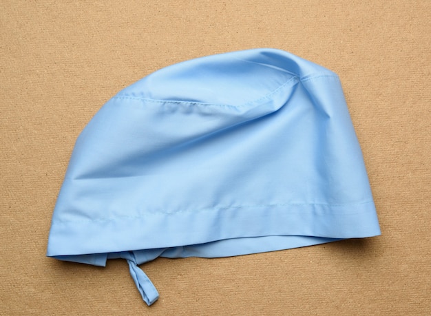 Blue textile medical cap with ties for doctor, surgeon on a brown background, top view