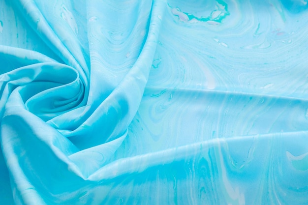 写真 ベースカラーのシルクの青い上面図、青い大理石のパターンのシルクの生地、波状、らせん状、折り目、渦巻き、背景、布の背景、テキストのコピースペースがあります