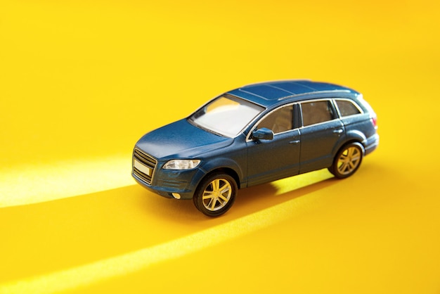 Blue toy off-road vehicle on a yellow background with long sun shadows. Delivery, taxi and vacation concept.