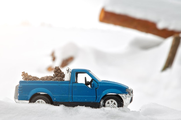 製材所の青いおもちゃのピックアップトラック雪の吹きだまりとおがくずで立ち往生後ろにモミの円錐形を運ぶ