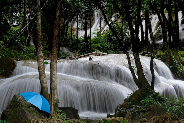 背景に柔らかな白い滝の小川と岩の上の青い傘