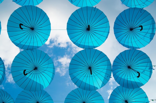 В солнечный день в небе плавают синие зонтики. Монтаж проекта Umbrella Sky. Праздник и фестивальное празднование. Тень и защита. Наружный художественный дизайн и декор.