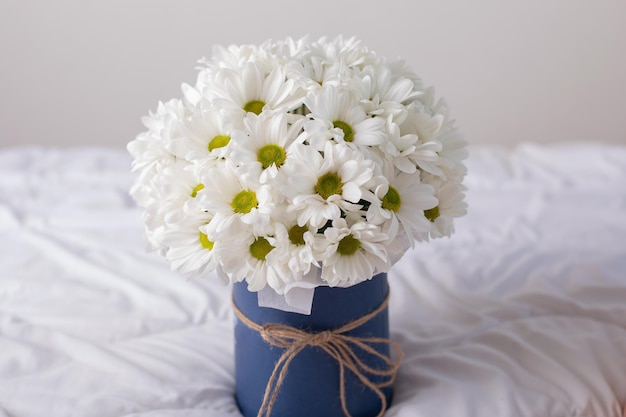 A blue vase with white flowers on a bed