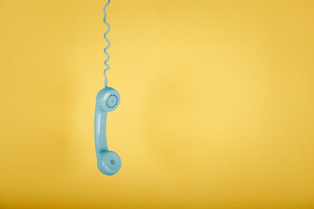 Blue vintage telephone hanging on yellow space