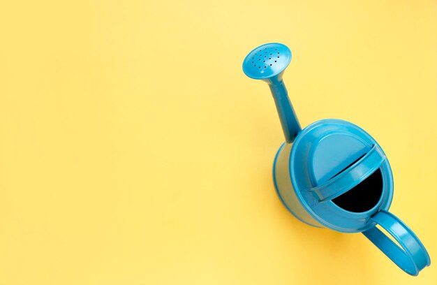 Blue watering can on yellow background Creative concept of investment growth success in business and life or hello summer Top view Flat lay