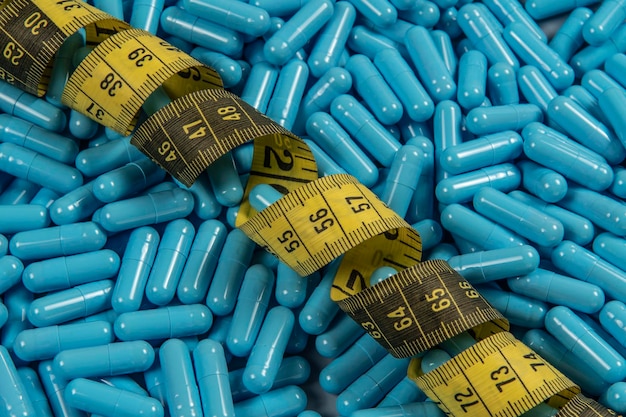 Photo blue weight loss pills and measuring tape symbolizing slimming