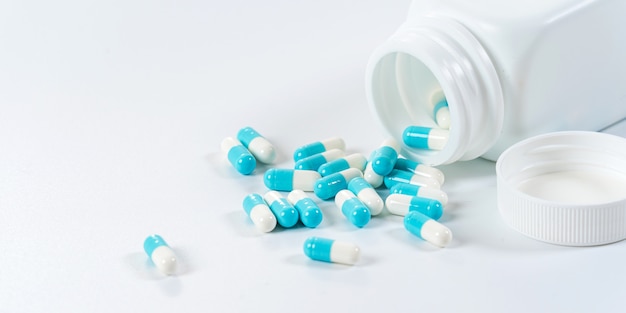 Синие и белые капсулы таблетки, льющиеся из бутылки на белом фоне
