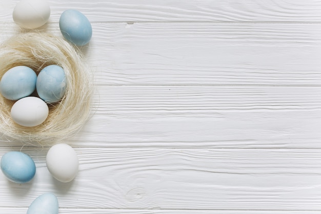 Blue and white Easter eggs in nest on white wooden background