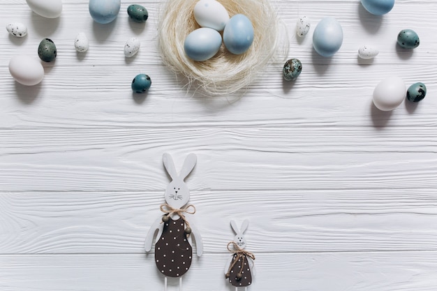 Blue and white Easter eggs in nest on white wooden background.