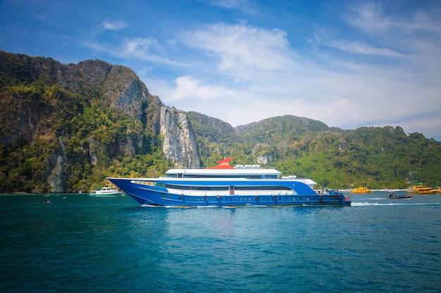 Photo blue and white passenger ferry ship sailing to destination point port with another ships mountain