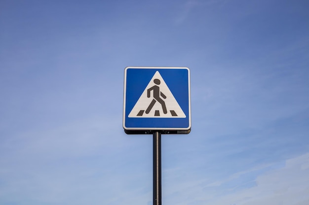 Синий и белый знак пешеходного перехода на фоне неба