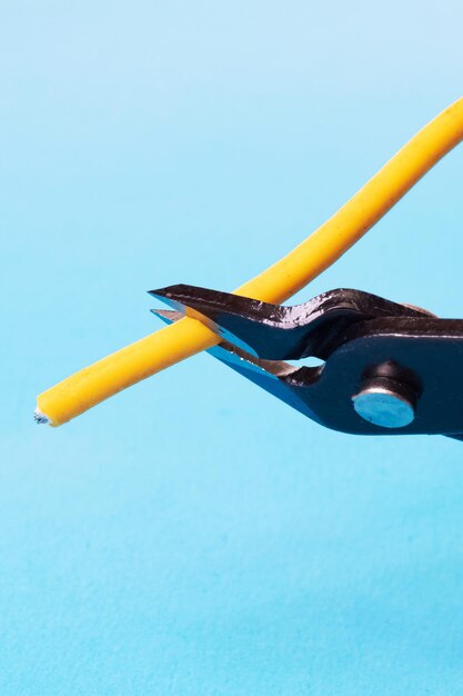 Blue wire cutter cuts yellow wire on blue background