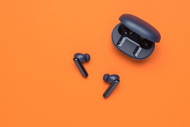 Blue wireless headphones with an open case on an orange background a popular wireless gadget