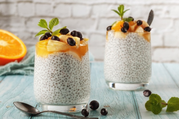 On a blue wooden table, chia pudding with banana in two glass glasses with raw chia seeds