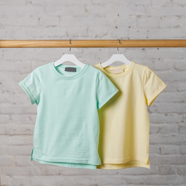 파란색과 노란색 아동용 티셔츠는 흰색 벽돌 벽 디자인 공백에 걸이에 걸려 있습니다.