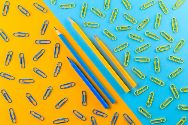 Blue and yellow colored pencils and paperclips in the blue and yellow background