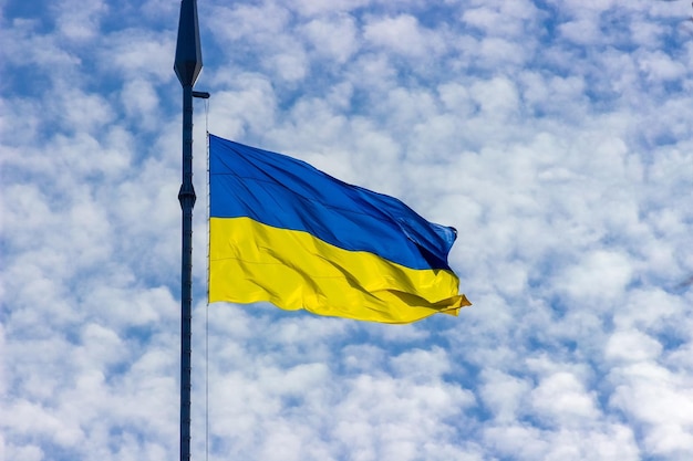 The blue yellow flag of Ukraine flies on a flagpole against a blue sky with clouds.