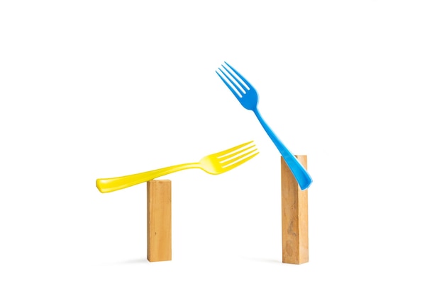 Blue and yellow plastic forks on wooden bricks on a white background with copy space