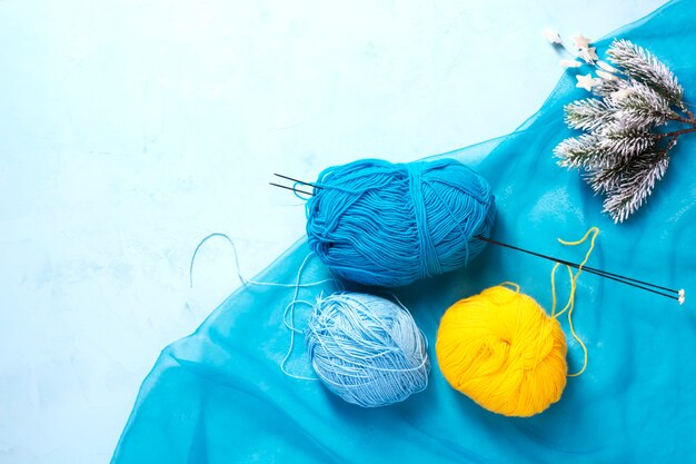 Blue and yellow yarn on a blue surface, next to snow-covered pine branches.