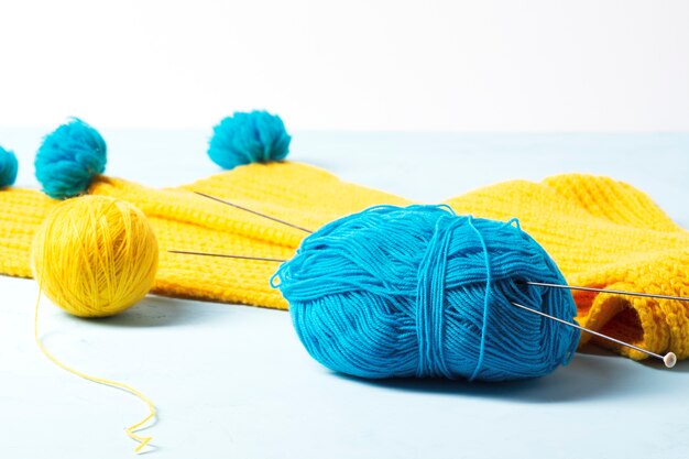 Blue and yellow yarn lies against the background of a yellow knitted scarf.