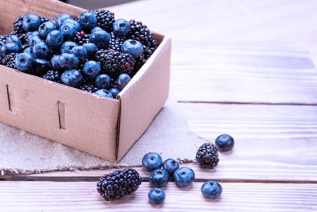 Blueberries and blackberries in a cardboard box on a wooden table Mixture of blue berries closeup