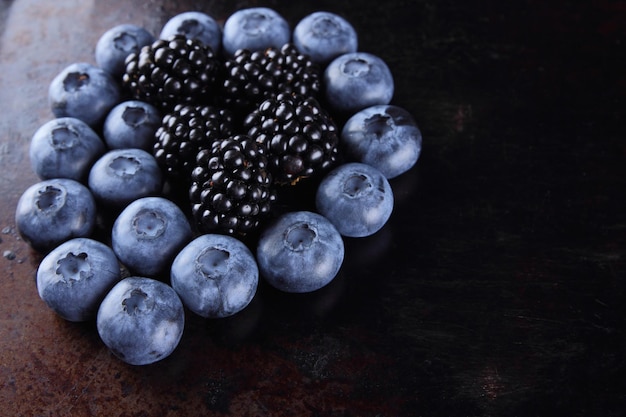 Голубые и черные ягоды на темном фоне Свежие ягоды на ржавом фоне