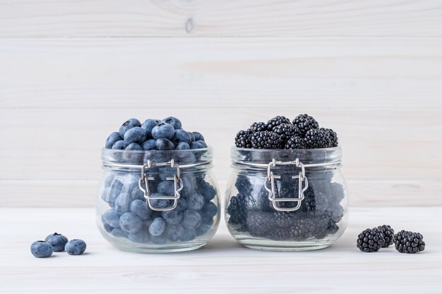 Blueberries and blackberries in a glass bowl on a wooden table, white board background.